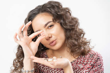 A beautiful young woman with curly long dark hair holds miniature sweet donuts in her hands and shows that she wants to eat themの写真素材