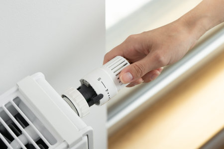The woman turns the regulator of the thermostatic valve of the radiator to the middle position to...