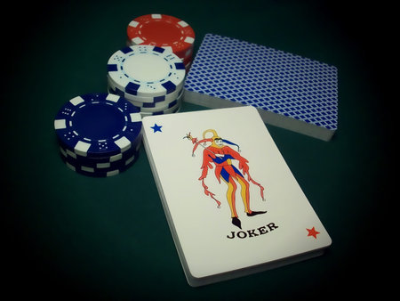 cut deck with joker showing up against red white and blue poker chips on a green table.