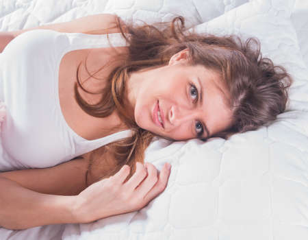 Beautiful young woman with blue eyes lying in the bedの写真素材