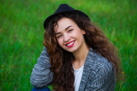 Joyful, curly-haired woman in a hat sees on the green grass.の写真素材