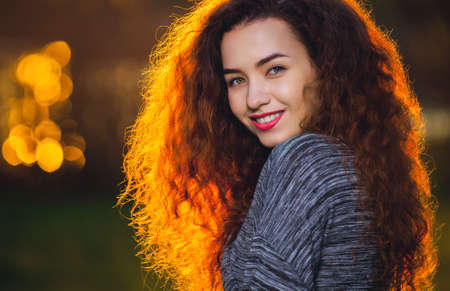 Smiling beautiful girl with curly, hair illuminated by the sun on a beautiful background of sunset.の写真素材