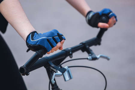 Hands of a girl in a sports blue-black gloves holding on to the steering wheel of the bicycle. Close-up.の写真素材