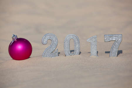 Four New Year's figures are in the sand on the beach or seaside, cast a large shadow on the ground. Near the sand is pink ball. New Year Celebration and Christmas in the ocean, the sea. Traveling.の写真素材