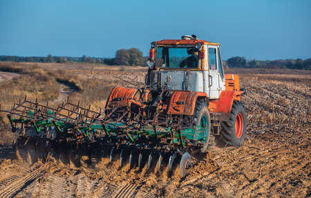 Large, old, beautiful tractor plowing the earth on the field after harvest autumn harvest sunflowers. Employment of agricultural equipment and machines.の写真素材
