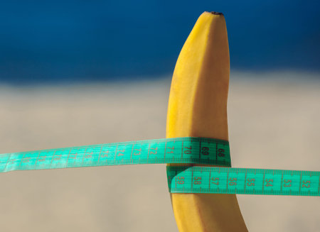 Banana with measuring tape stretched on the beach. The concept of reduction of excess weight and a...