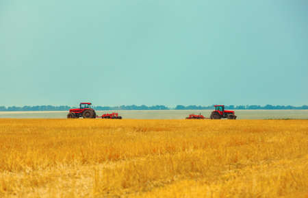 Summer day two  tractors to plow, plow the soil on sloping, wheat. Agricultural land treatment before planting.の写真素材