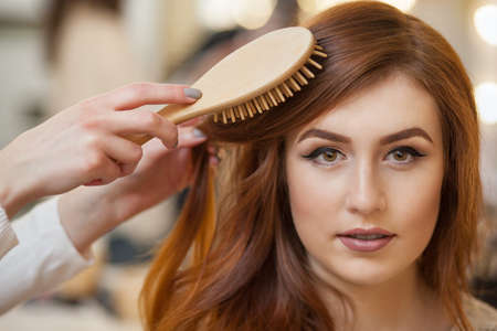Hairdresser combing her long, red hair of his client in the beauty salon. Professional hair care and creating hairstyles.の写真素材
