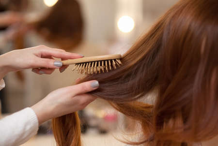 Hairdresser combing her long, red hair of his client in the beauty salon. Professional hair care and creating hairstyles.の写真素材