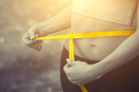 Sport girl measuring waist with yellow measuring tape. Reducing excess weight. Healthy lifestyle.