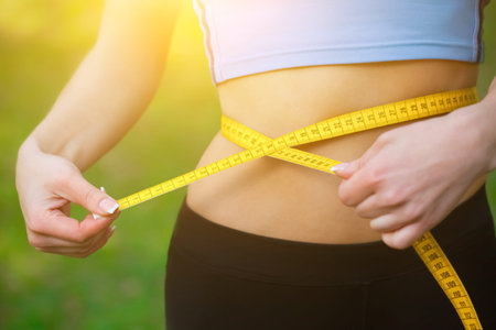 Sport girl measuring waist with yellow measuring tape. Reducing excess weight. Healthy lifestyle.