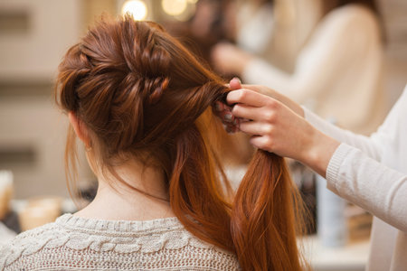 Beautiful, with long, red-haired hairy girl, hairdresser weaves a French braid, in a beauty salon....