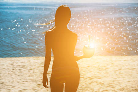 An attractive, young girl holding a coconut to drink while relaxing at a resort near the ocean.の写真素材
