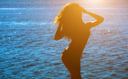 Silhouette of a beautiful, slender girl with curly hair on the background of sunset by the sea on the beach.の写真素材