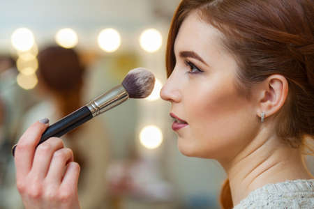 Make-up artist puts powder on the face of a beautiful, red-haired girl in the beauty salon. Professional cosmetics, make-up and skin care.の写真素材