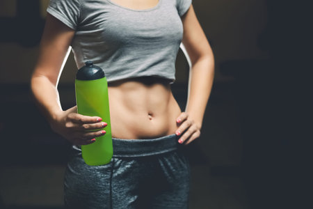 Slim girl bodybuilder, holding a bottle of water while exercising in the gym. Sports concept, fat...