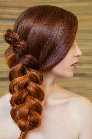 Beautiful girl with long red hair, braided with a French braid, in a beauty salon. Professional hair care and creating hairstyles.の写真素材