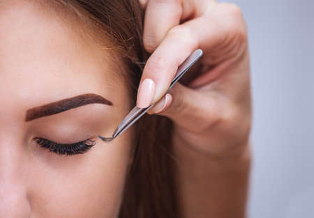 Makeup Master corrects, and strengthens eyelashes beams, holding out a pair of tweezers in a beauty salon. Professional care for the skin and eyes.の写真素材