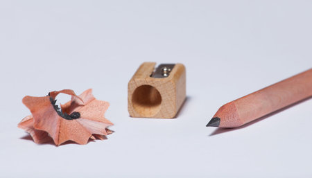 A wooden simple pencil, a pencil sharpener and shavings lie on a white isolated background.