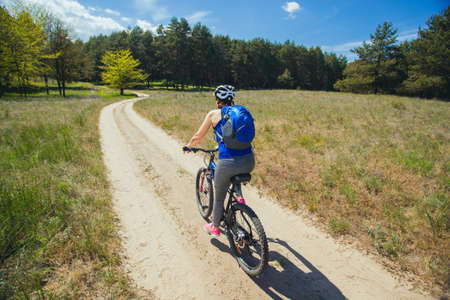 One young woman - an athlete rides on a mountain bike outside of town in a pine forest, on a summer day.の写真素材