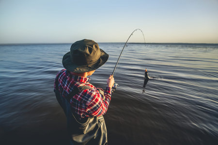 A fisherman with a fishing rod in his hand and a fish caught stands in the waterの写真素材