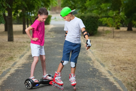 Two kids boy on roller skates and girl on self-balancing scooter wrapped in park