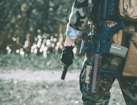 The soldier in the performance of tasks in camouflage and protective gloves holding a gun. War Zone.の写真素材