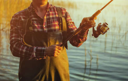 A fisherman in a red shirt is fishing for spinning in a freshwater pond at sunset.の写真素材