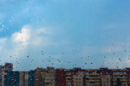Water drops flow down on the glass in the rain on a blue backgroundの写真素材
