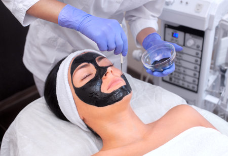 The procedure for applying a black mask to the face of a beautiful woman. Spa treatments and care of...