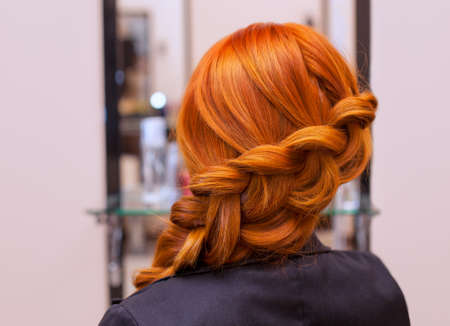 Beautiful girl with long red hair, braided with a French braid, in a beauty salon. Professional hair care and creating hairstyles.の写真素材