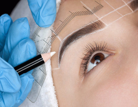 Permanent make-up for eyebrows of beautiful woman with thick brows in beauty salon. Closeup...