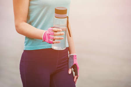 A sportswoman holds a glass bottle of water in her hand during a sports training session.の写真素材