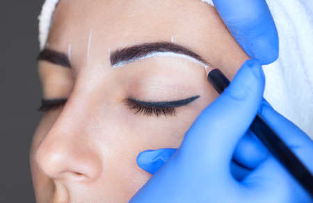 Permanent make-up for eyebrows of beautiful woman with thick brows in beauty salon. Closeup beautician doing  tattooing eyebrow.の写真素材