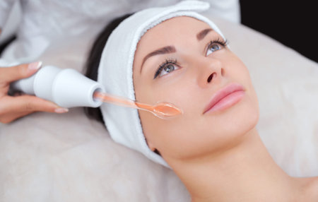 The cosmetologist makes the procedure Microcurrent therapy of the facial skin of a beautiful, young...