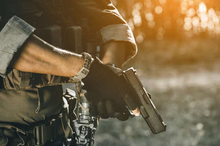 the soldier in the performance of tasks in camouflage and protective gloves holding a pistol. War Zone.の写真素材