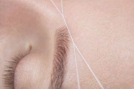 The make-up artist plucks her eyebrows with a thread close-up. Face care beauty treatments in the beauty salon.の写真素材