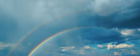 Primary and secondary rainbow in the background of thunderclouds and rain.の写真素材