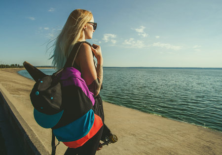 Beautiful, sexy white blonde with blue hair in tattoos with long board on a sunset background by the sea.の写真素材