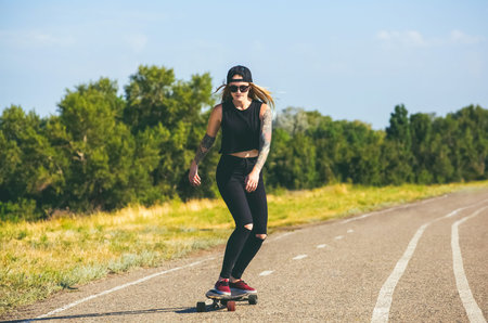 A beautiful, sexy hipster blonde with blue hair in tattoo ride a longboard  on the street.の写真素材
