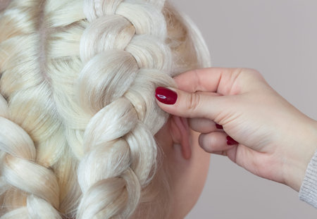 Beautiful girl with blonde hair, hairdresser weaves a  braid close-up, in a beauty salon....