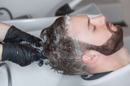 The hairdresser washes the head of the young man with shampoo after haircuts in the hairdresser.の写真素材