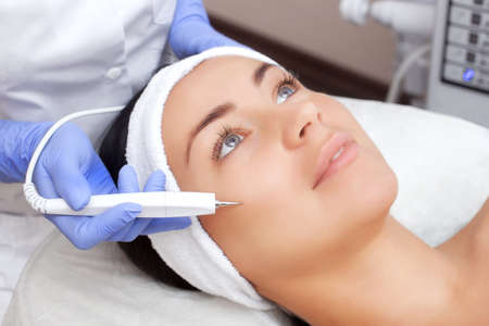 The cosmetologist makes the procedure treatment of Couperose of the facial skin of a beautiful, young woman in a beauty salon.Cosmetology and professional skin care.の写真素材