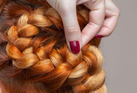 Beautiful girl with red hair, hairdresser weaves a  braid close-up, in a beauty salon. Professional hair care and creating hairstyles.の写真素材
