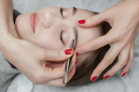 Master makeup corrects, and gives shape to pull out with forceps previously painted with henna eyebrows in a beauty salon. Professional care for face.の写真素材