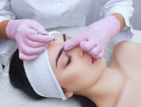 The doctor cosmetologist makes the Rejuvenating facial injections procedure for tightening and smoothing wrinkles on the face skin of a beautiful, young woman in a beauty salon.Cosmetology skin care.の写真素材
