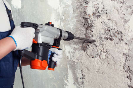 The builder with hammer drill perforator equipment making hole in wall at construction site.の写真素材