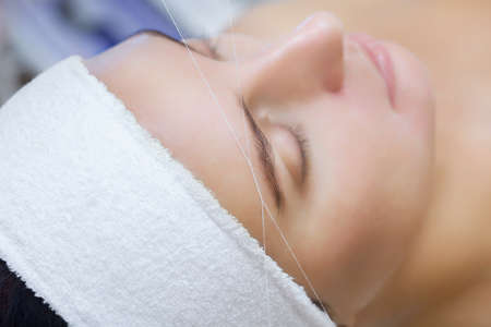 The make-up artist plucks her eyebrows with a thread close-up. Face care beauty treatments in the beauty salon.の写真素材
