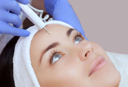 The cosmetologist makes the procedure treatment of Couperose of the facial skin of a beautiful, young woman in a beauty salon.Cosmetology and professional skin care.の写真素材