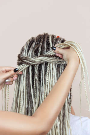 A hairdresser weaves dreadlocks to a beautiful young girl in a hairdresser's.の写真素材